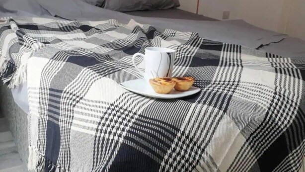 A bed with a checkered blanket, a white mug, and two pastries on a plate. - Immaculate 1-bed Apartment in Sheffield (Sheffield)