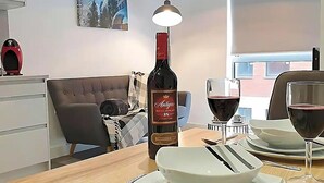 A dining area with a table set for two, a bottle of wine, and a window with a view of buildings. - Immaculate 1-bed Apartment in Sheffield (Sheffield)