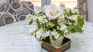Ett vitt bord med en vas med vita blommor, gardiner och utsikt över en pool.