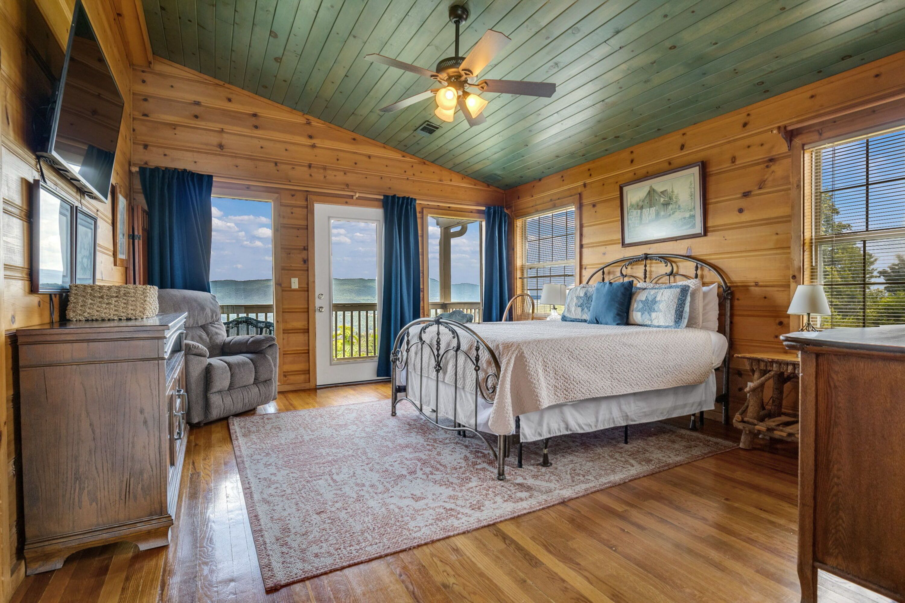 A wooden cabin bedroom with a bed, a chair, a desk, and a view of the ocean.
