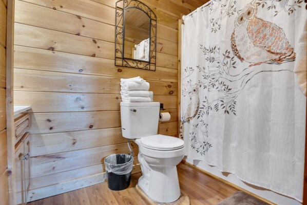 A wooden cabin bathroom with a toilet, a mirror, and a shower curtain with a bird design.