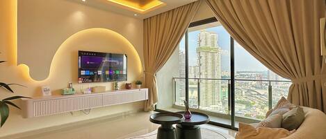 A modern living room with a flat-screen TV mounted on the wall, a sofa, a coffee table, and a view of a cityscape through large windows.