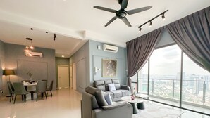 A modern living room with a grey sofa, a dining area with a table and chairs, and a large window with a city view.