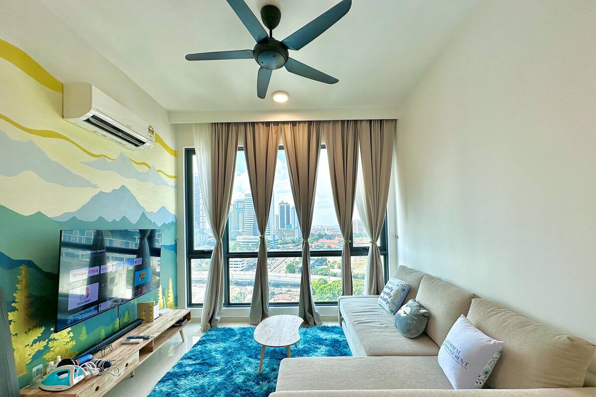 Un salon moderne doté d’un téléviseur à écran plat, d’un ventilateur de plafond, d’un canapé et offrant une vue sur le paysage urbain grâce à de grandes fenêtres.