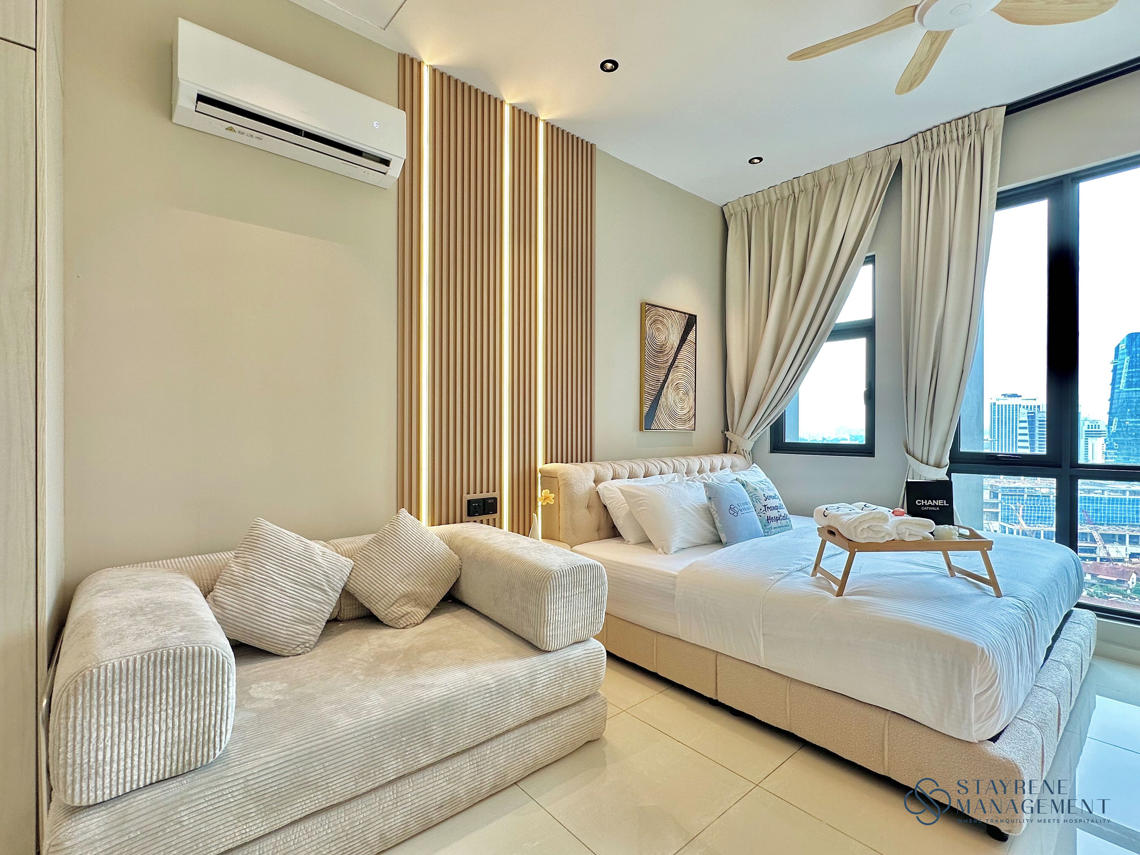 A modern hotel room with a sofa, a bed, a bedside table with towels, and a city view.