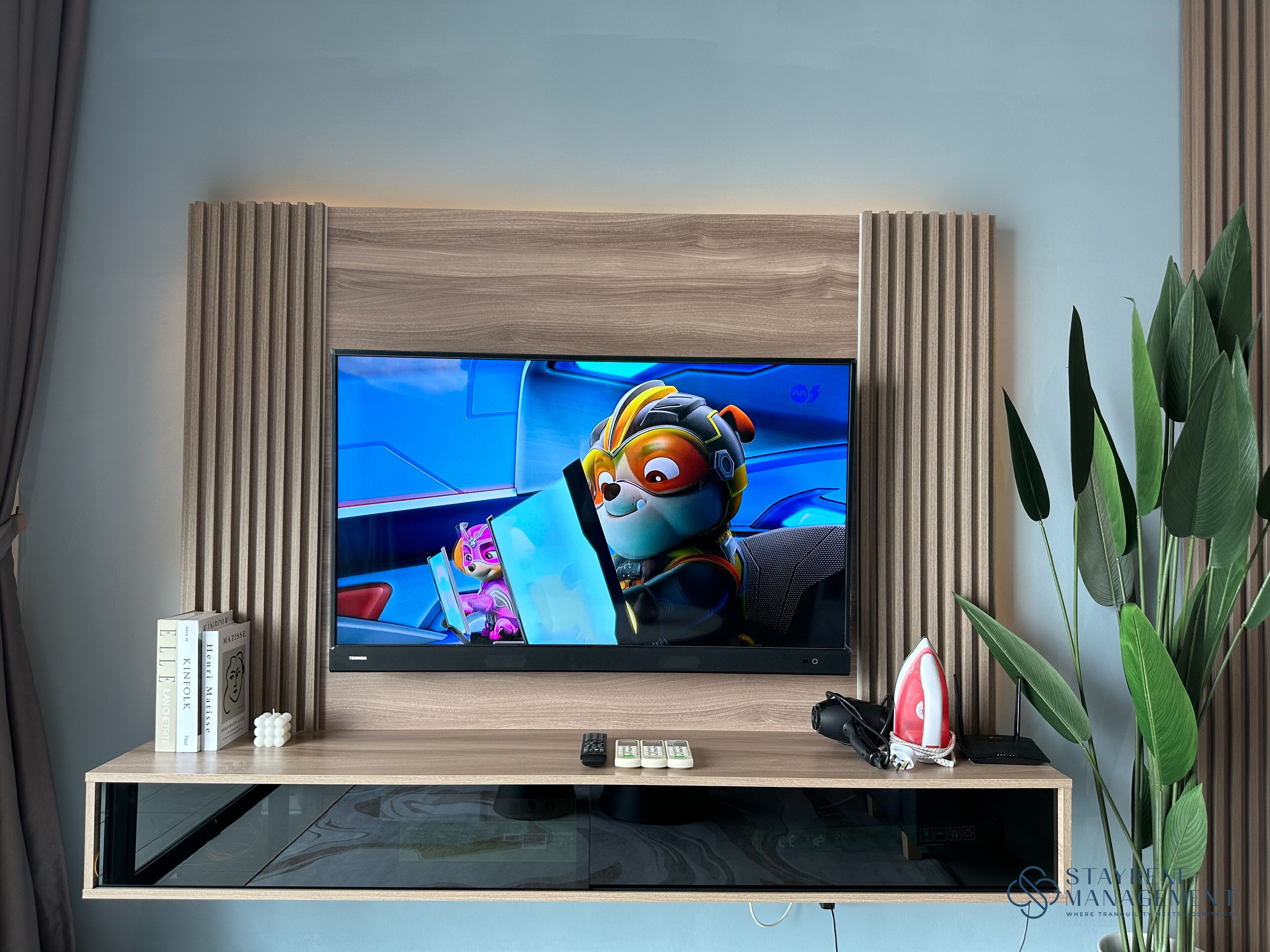 A flat-screen TV mounted on a wooden TV stand with a remote, a camera, and a pair of headphones.