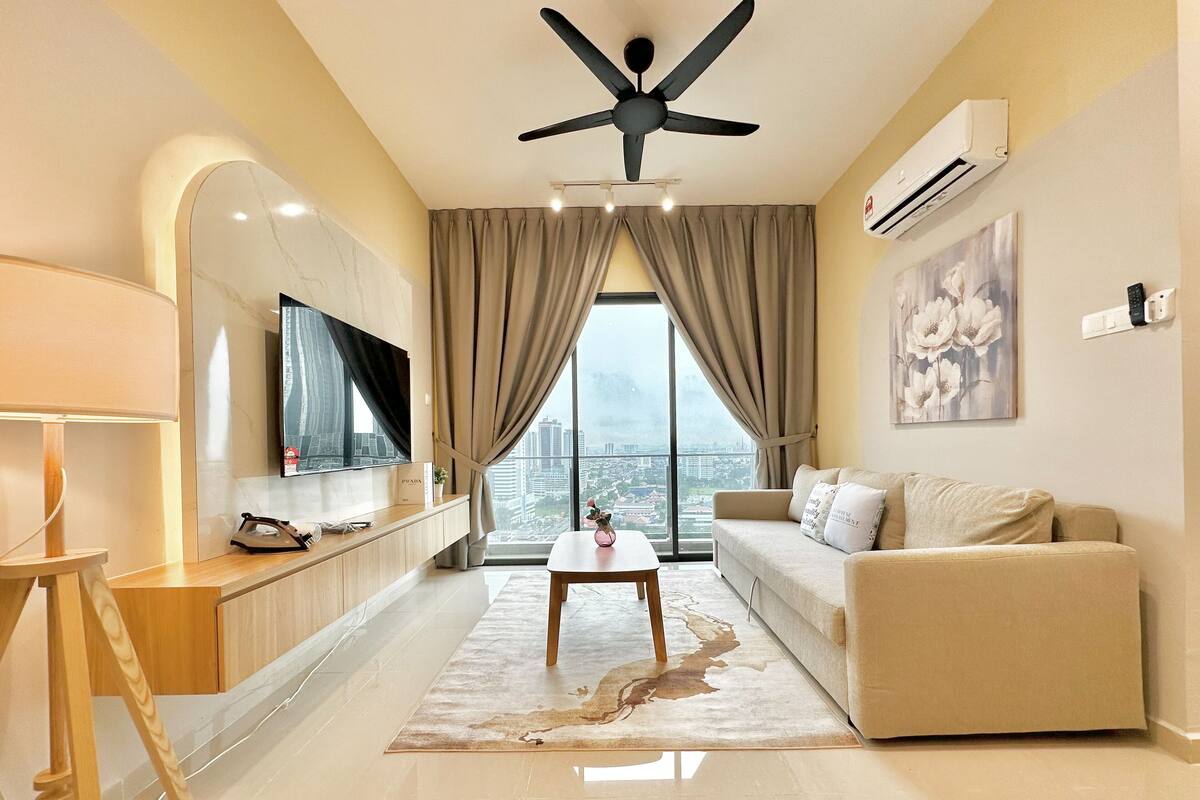 Un salon moderne doté d’un téléviseur à écran plat, d’un ventilateur de plafond, d’une grande fenêtre avec des rideaux, d’un canapé et d’une table basse.
