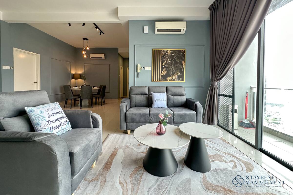Un salon moderne avec des canapés gris, un coin repas et une grande fenêtre avec des rideaux.