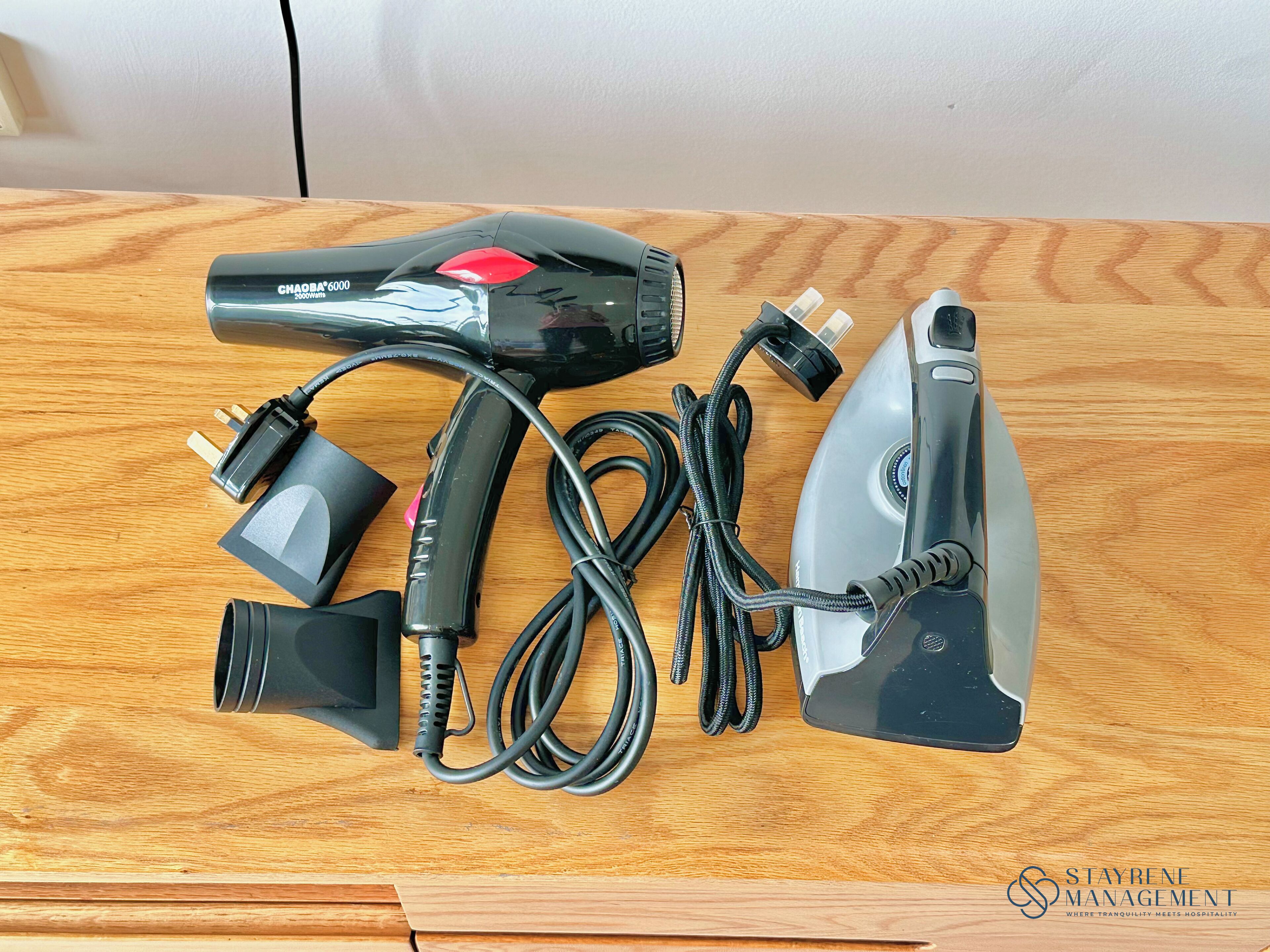 A hair dryer, its power cord, and a plug adapter on a wooden surface.