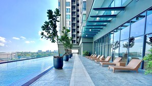 A rooftop pool area with lounge chairs and potted plants, overlooking a cityscape.
