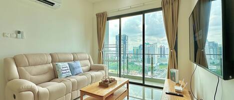 A modern living room with a beige sofa, a wooden coffee table, a ceiling fan, and a large window offering a city view.