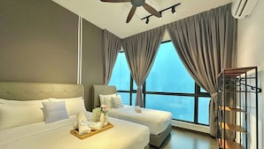 A hotel room with two beds, a ceiling fan, large windows with curtains, and a wooden shelf unit.