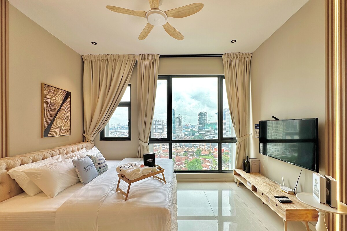 A modern hotel room with a large bed, a flat-screen TV, a desk, and a view of the cityscape.