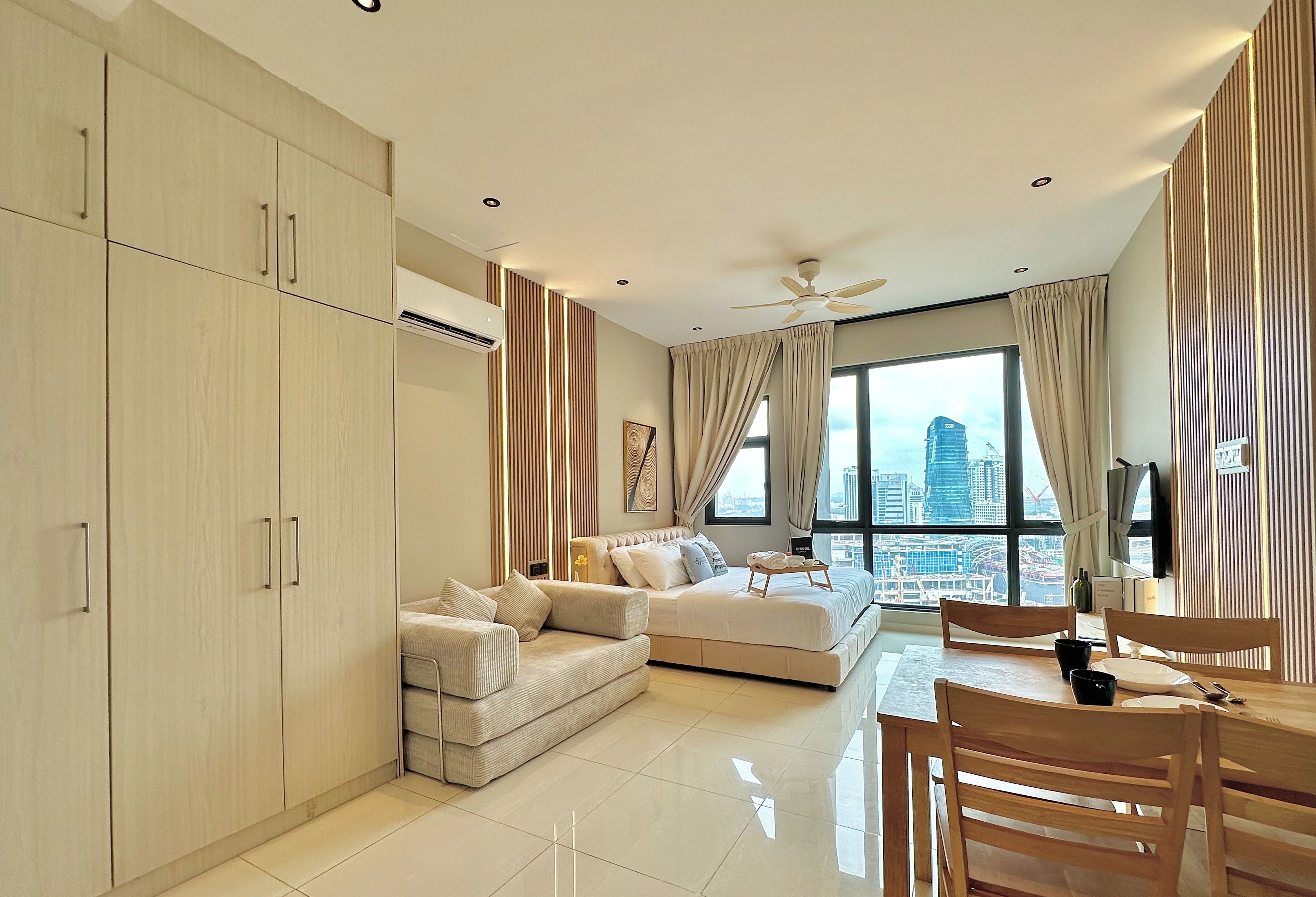 A modern living room with a sofa, a dining table, and a city view through large windows.