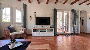 Un saló amb televisió, un sofà, una taula de centre de fusta i una porta corredissa de vidre que dona a una zona exterior.
