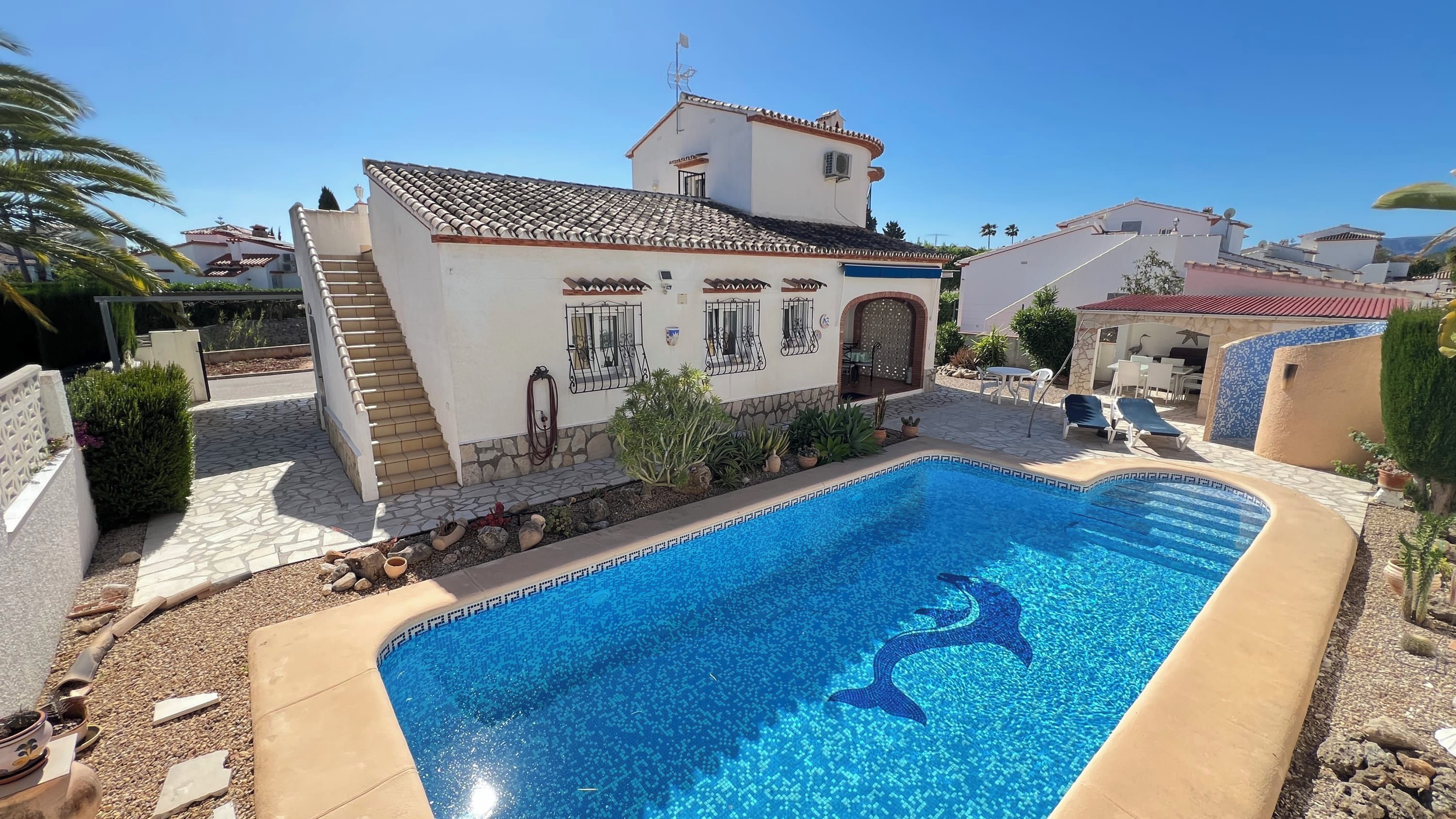 A swimming pool with a decorative tile border, a building with a tiled roof, and a stone pathway.