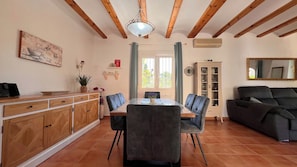 Una zona de menjador amb sostre de fusta, taula de dinar amb cadires, un armari i un sofà.