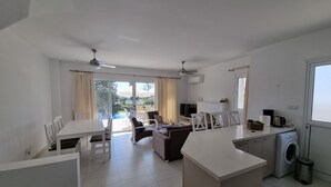 A modern, well-lit living area with a dining table, sofas, and a kitchen area including a washing machine. - Seaview 4 Bedroom villa with pool (Paphos)