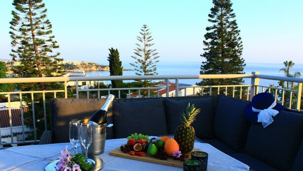 A balcony with a table set for a meal, featuring a fruit platter, wine glasses, and a bottle. - Seaview 4 Bedroom villa with pool (Paphos)