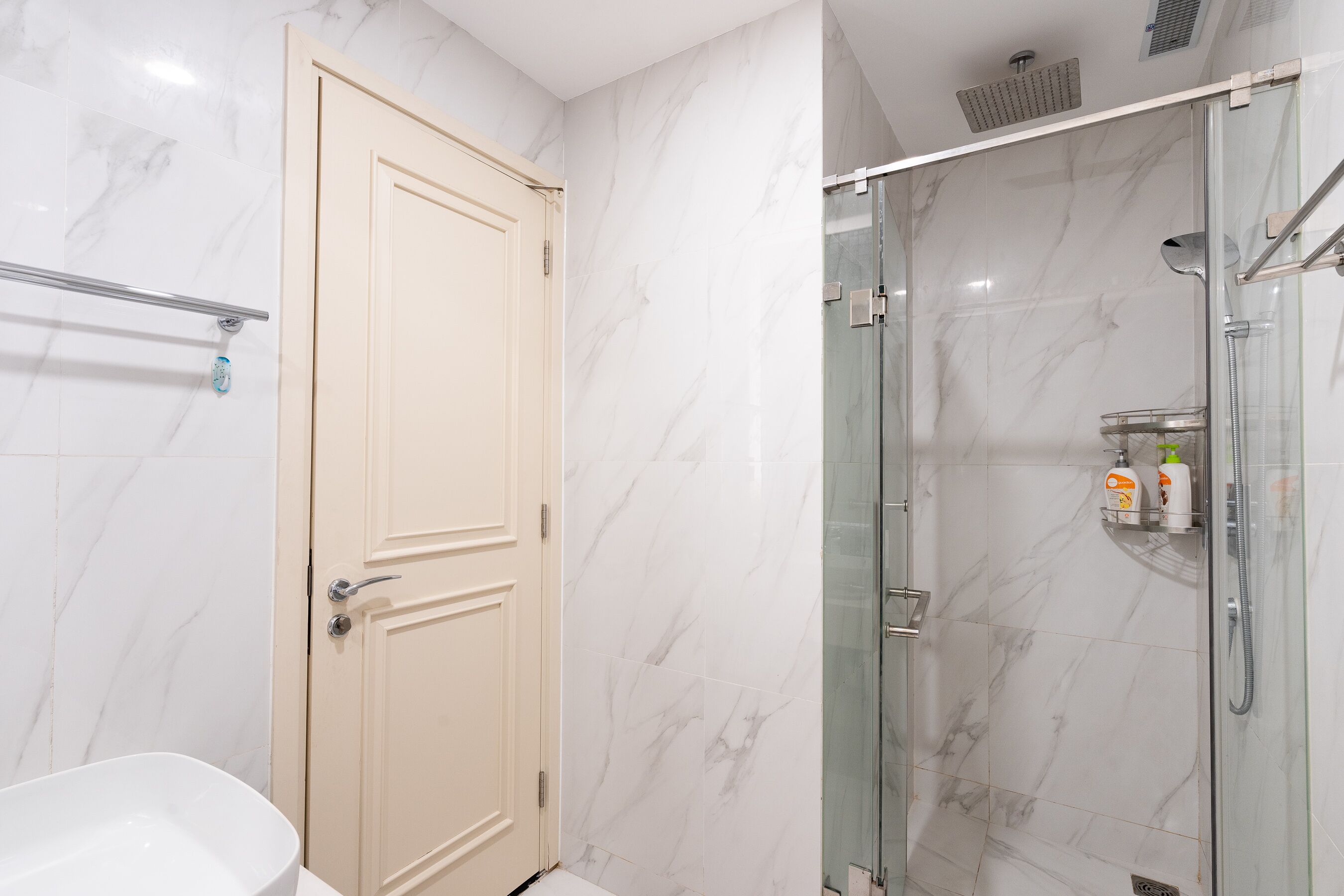 A bathroom with a marble wall, a glass shower enclosure, and a beige door.