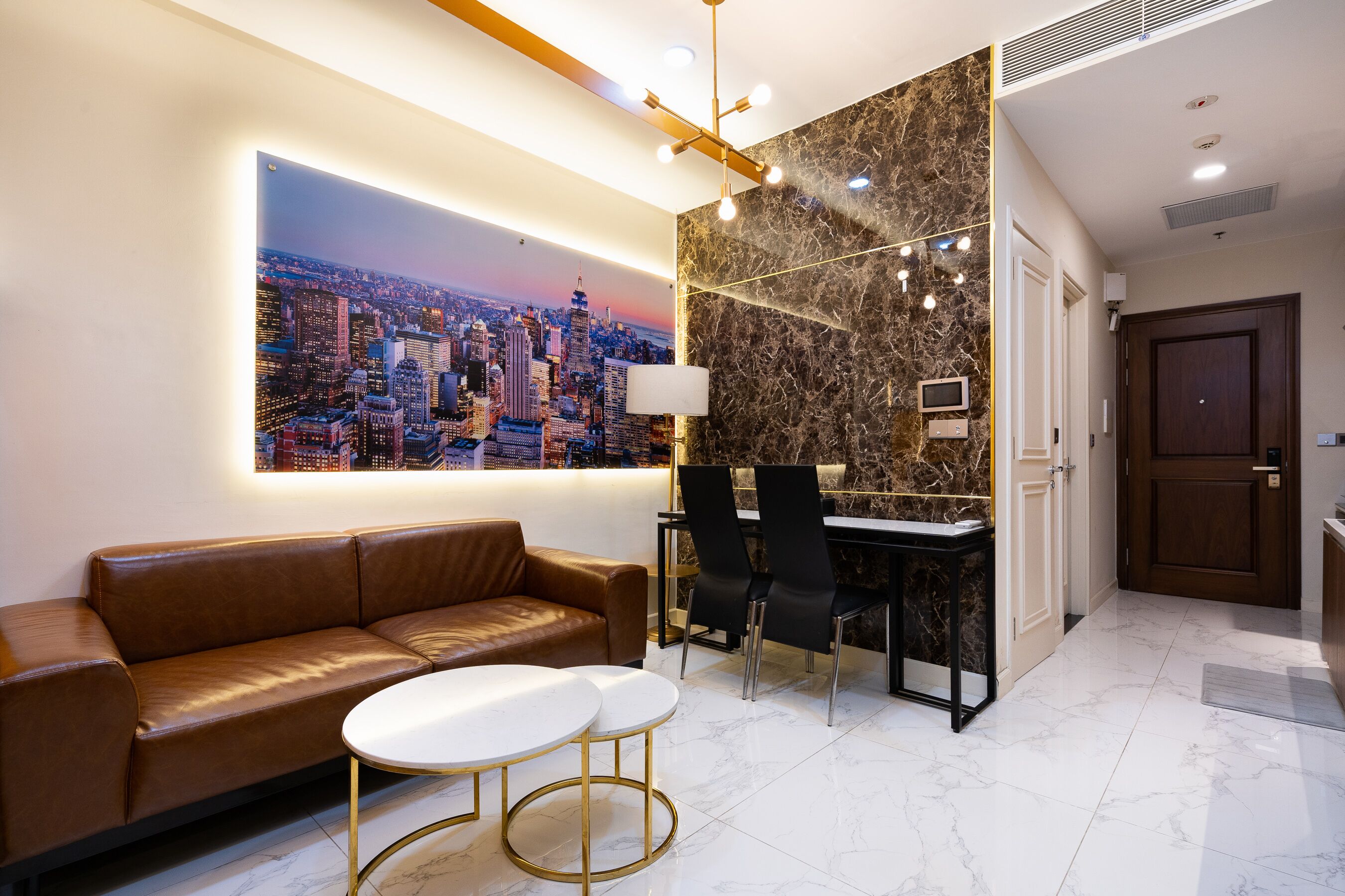 A modern hotel lobby with a leather sofa, a dining area with a marble table, and a cityscape mural.
