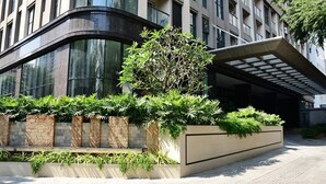 Un edificio moderno con fachada curva, amplios ventanales y un jardín ajardinado con diversas plantas.