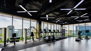 Un gimnasio moderno con diverso equipo de ejercicio, amplias ventanas y vistas a la ciudad.
