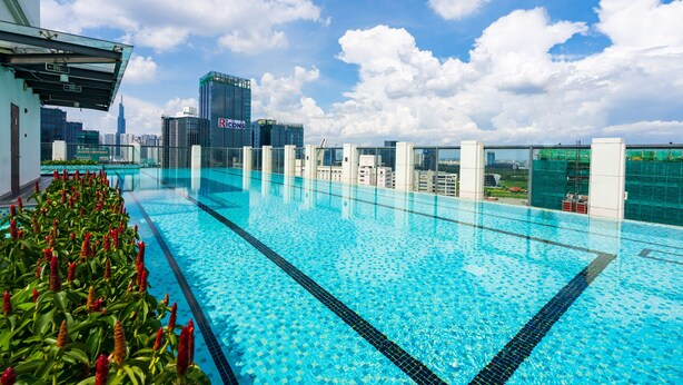 Una piscina infinita en la azotea con vista al horizonte de la ciudad, rodeada de edificios modernos y un cielo despejado.