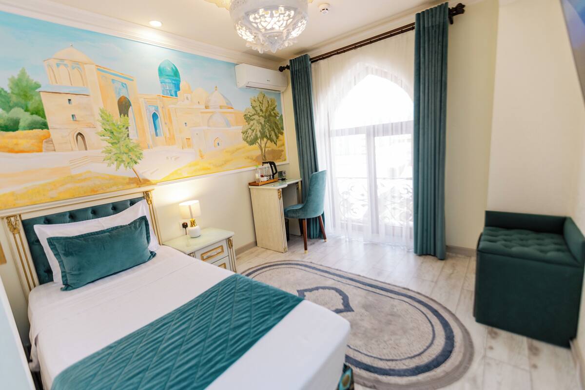 A hotel room with a large bed, a desk, a chair, a small table, and a window with curtains.