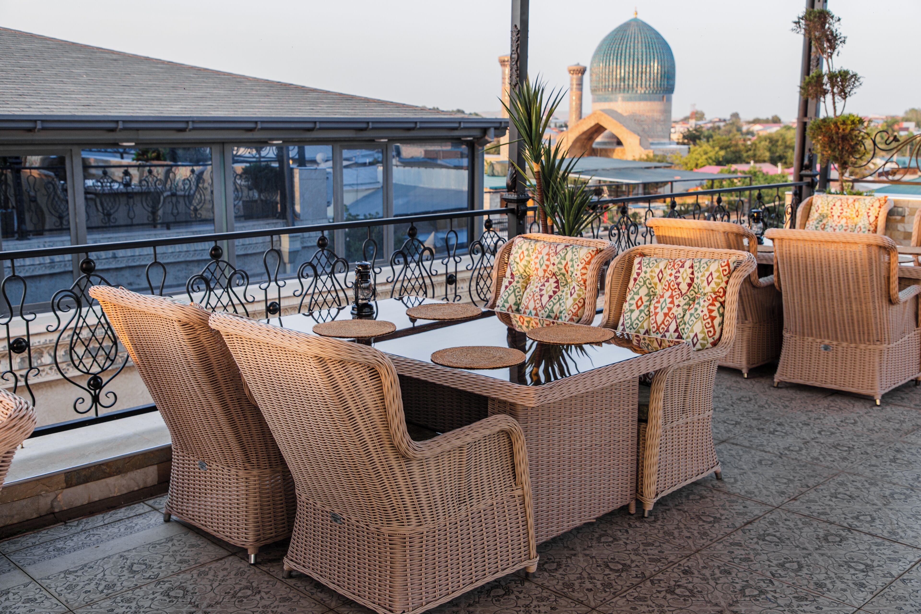 Mueble de mimbre con una mesa y sillas de vidrio en una terraza que ofrece vistas a una cúpula y edificios.