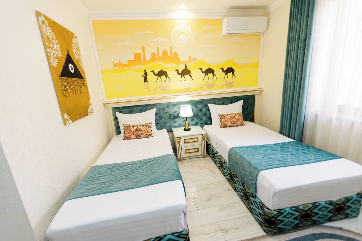 A hotel room with two beds, a nightstand, a lamp, and a mural on the wall.