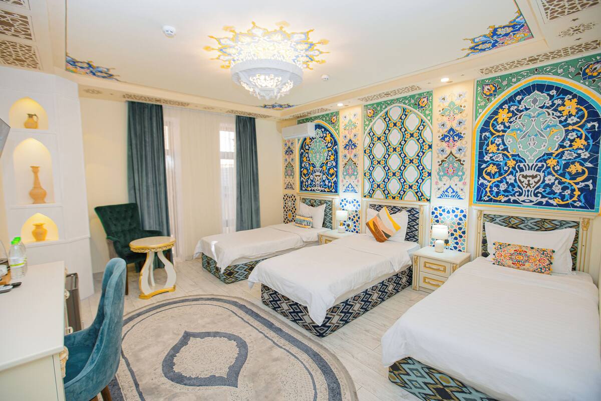A hotel room with two beds, a desk, a chair, a small table, and a chandelier.