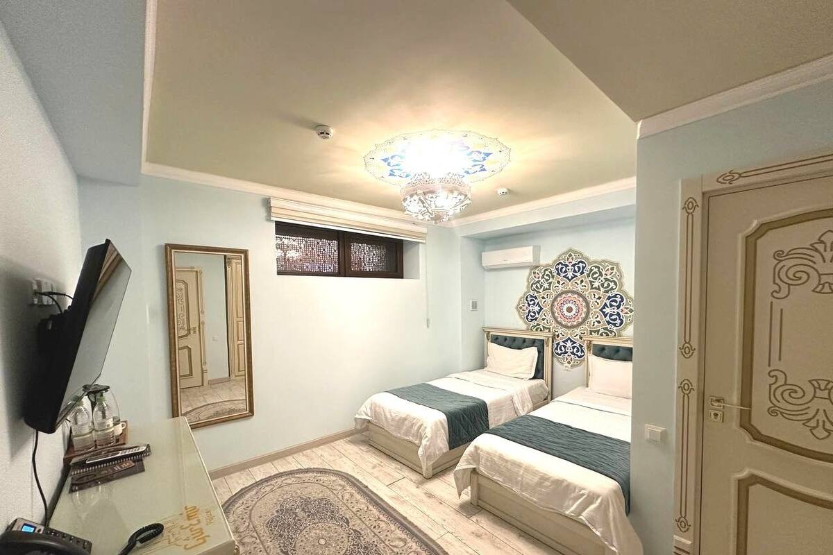 A bedroom with two beds, a television, a decorative mirror, and a patterned rug.
