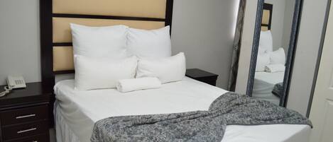 A neatly made bed with white linens and a patterned throw blanket, a bedside phone, and a mirror on the wall.