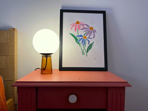 A framed artwork of flowers on a pink dresser with a round table lamp beside it. - Bel Appartement Haussmannien à Montparnasse (Paris)