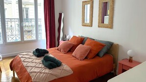 A bedroom with a bed, a bedside table, a lamp, and a window with curtains. - Bel Appartement Haussmannien à Montparnasse (Paris)