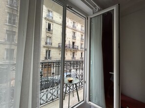 A room with a large window overlooking a street with cars and a building with balconies. - Bel Appartement Haussmannien à Montparnasse (Paris)