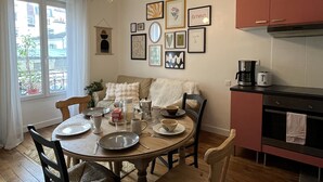 A dining area with a round table set for four, surrounded by chairs. A kitchen with red cabinets and a coffee maker is visible to the right. - Bel Appartement Haussmannien à Montparnasse (Paris)