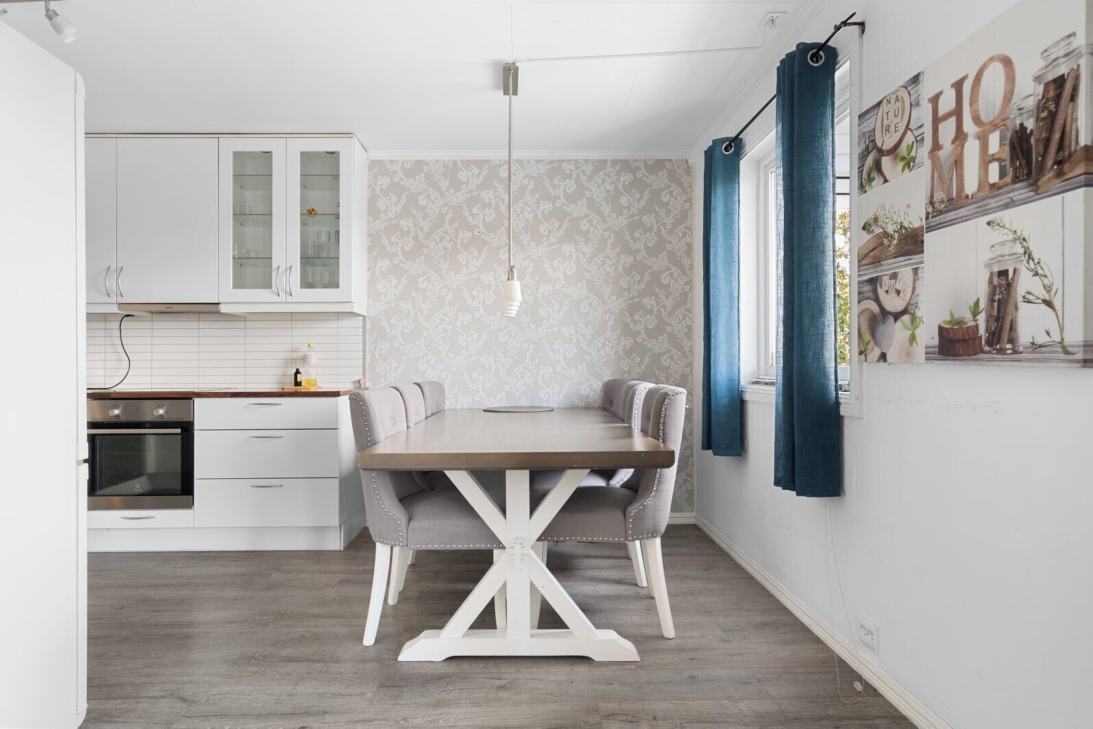 A modern kitchen with white cabinets, a wooden dining table, and blue curtains.