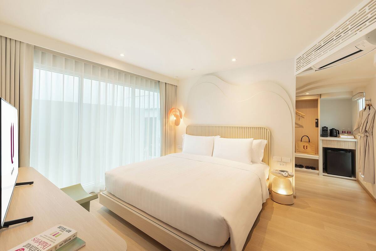 Une chambre d’hôtel moderne dotée d’un grand lit, d’un bureau avec un ordinateur portable, d’une coiffeuse avec un miroir et d’une salle de bain avec douche.