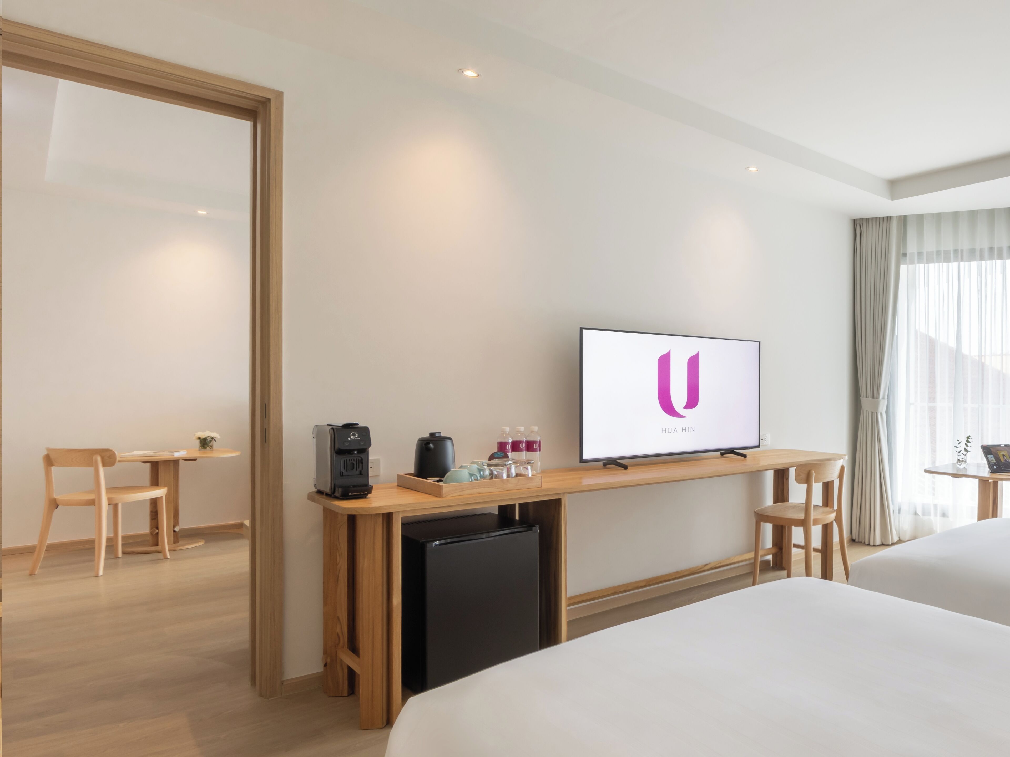 A hotel room with a bed, a desk with a television, a coffee machine, and a small refrigerator.