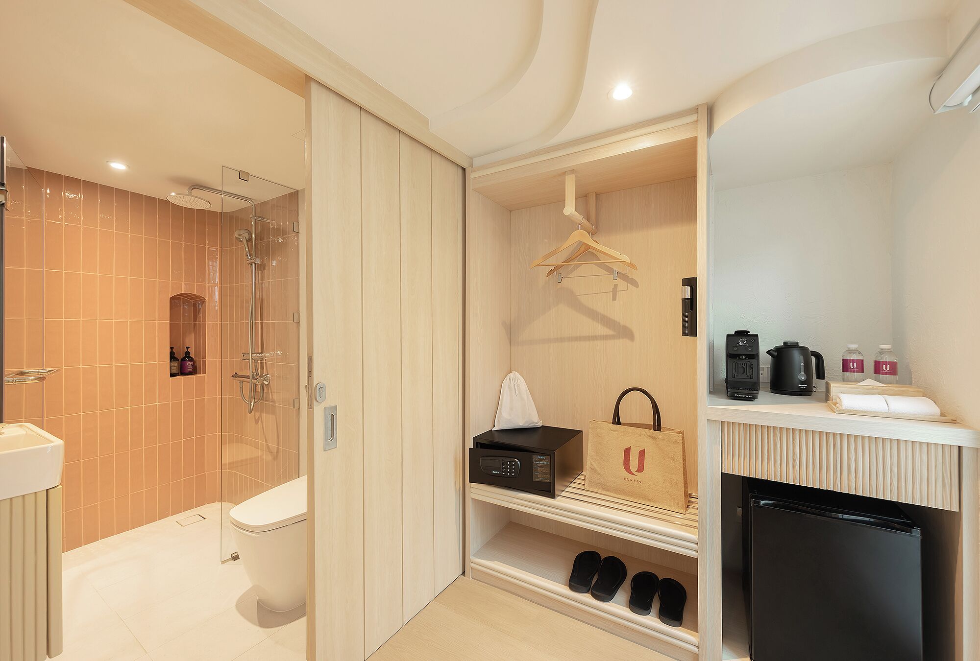 Een moderne badkamer met een douche, toilet en een wastafelmeubel. Er is een plank met een tas eroverheen en een kleine koelkast.