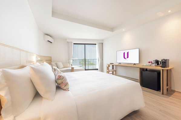 Una habitación de hotel con una cama grande, un escritorio con ordenador, cafetera y televisión.