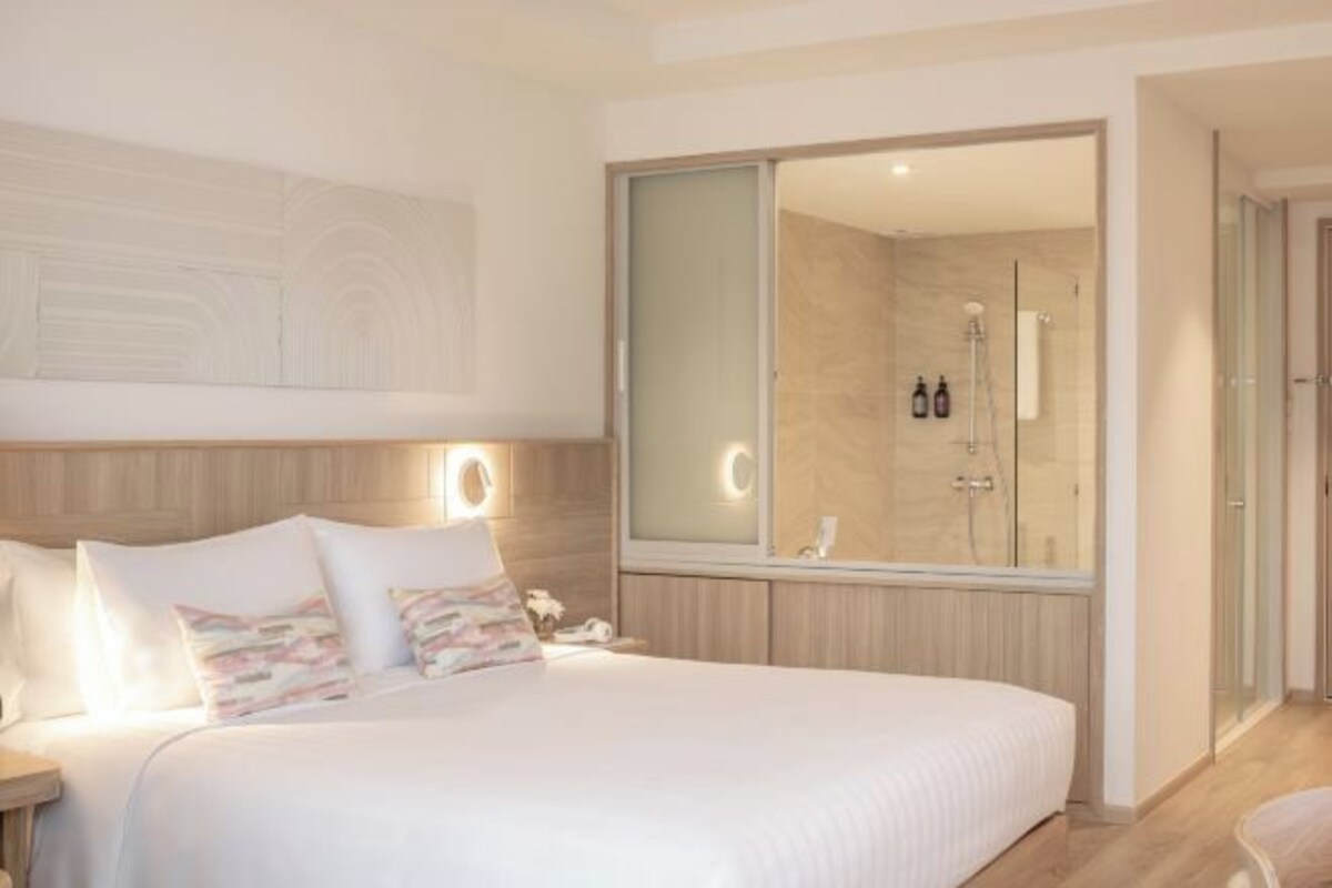 A modern hotel room with a large bed, bedside lamps, a large mirror, and a shower area.