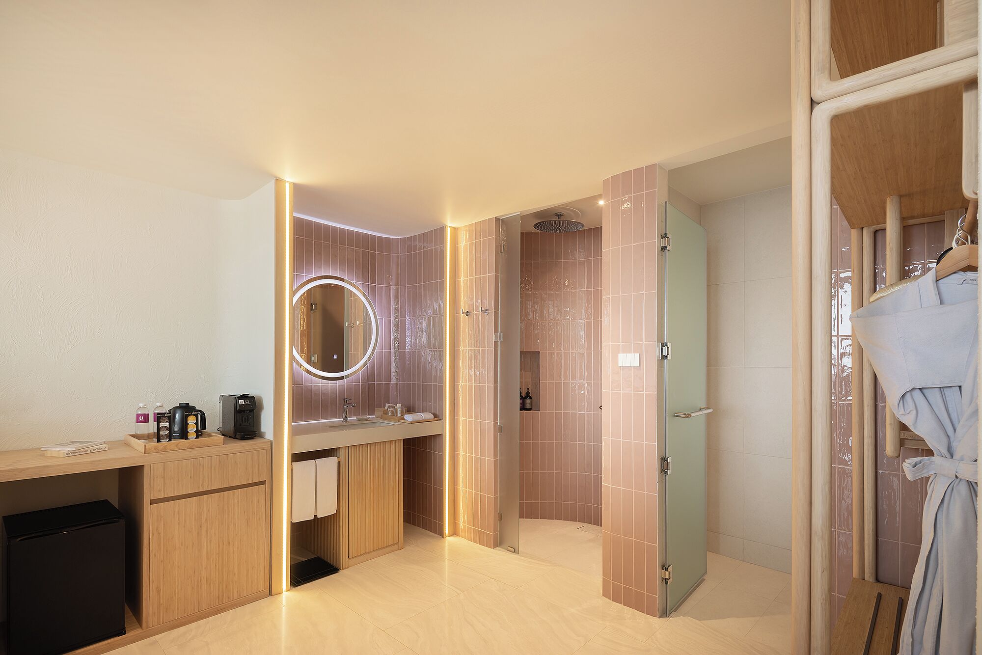 A modern bathroom with a vanity, a mirror with a light, a shower area, and a robe hanging.