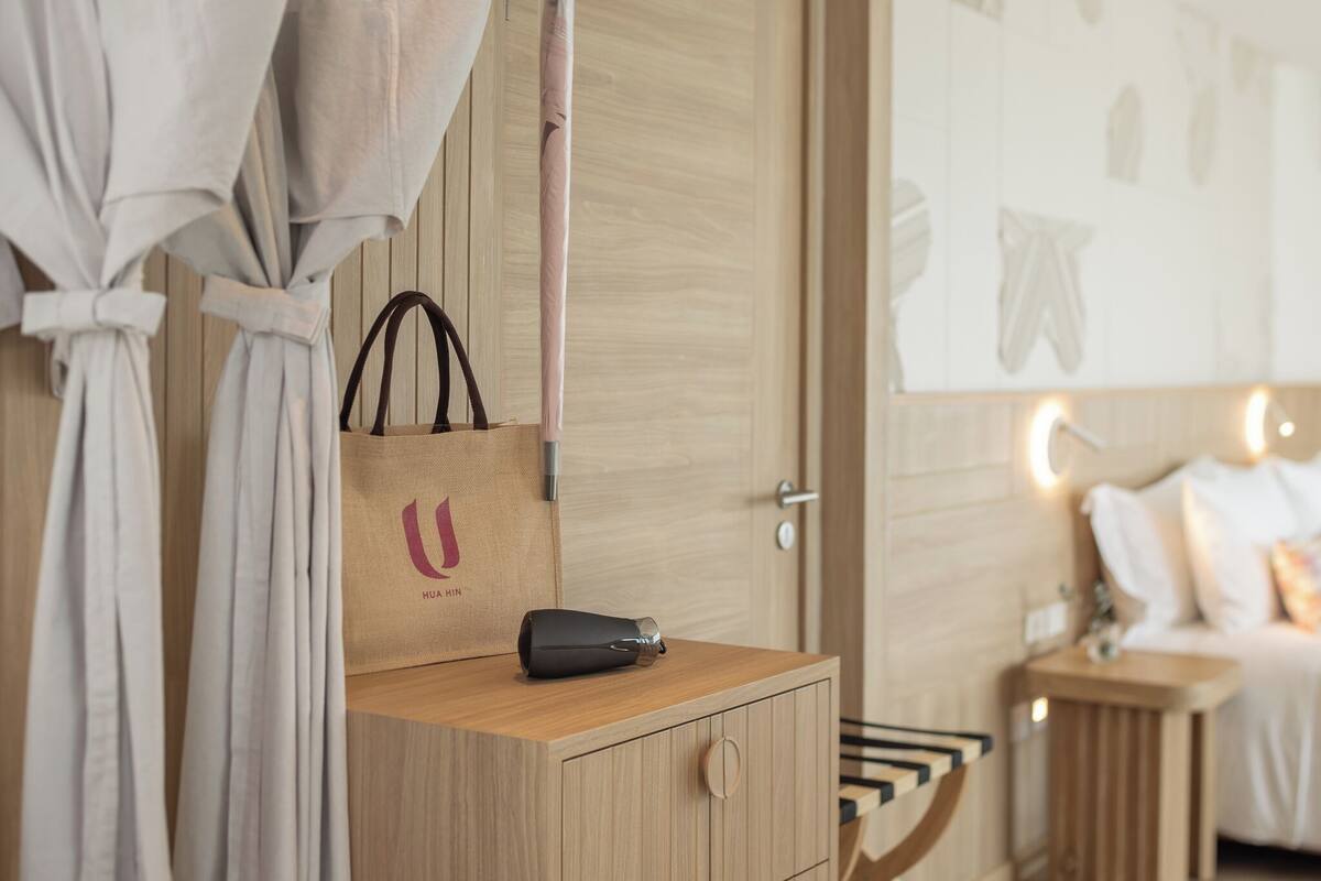 Une table de chevet en bois, avec un sac à main noir et un sac en papier marron orné d’un logo.