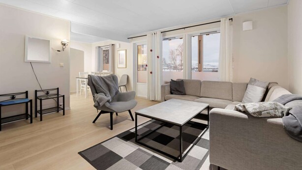 A modern living room with a sofa, armchair, coffee table, and a view of the outdoors through large windows. - Lovly 3 Bedroom Apartment With the View of Aurora (Tromsø)