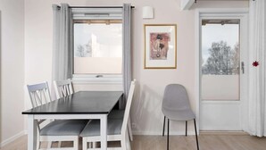 A dining area with a table and chairs, a window with curtains, a framed picture on the wall, and a door with a view outside. - Lovly 3 Bedroom Apartment With the View of Aurora (Tromsø)