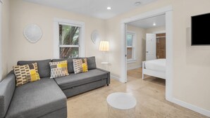 A modern living room with a grey sofa, a round coffee table, and a bed in the adjacent room.