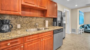 Cocina con encimeras de granito, armarios de madera y electrodomésticos de acero inoxidable, incluyendo un lavavajillas.